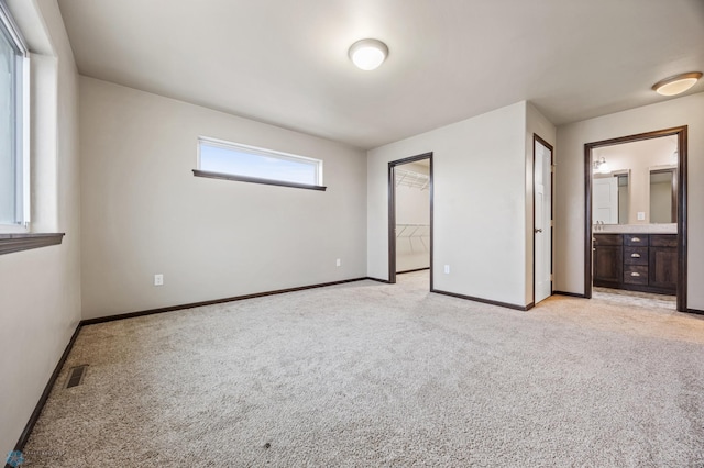 unfurnished bedroom with ensuite bathroom, a walk in closet, light carpet, and a closet