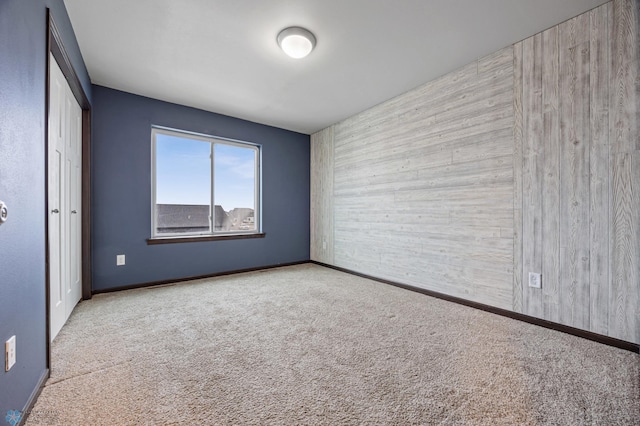 unfurnished bedroom with light carpet, wooden walls, and a closet