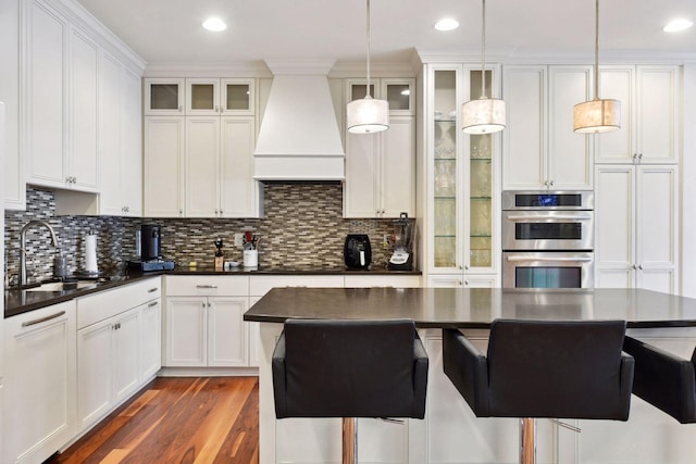 kitchen with pendant lighting, premium range hood, white cabinetry, and sink