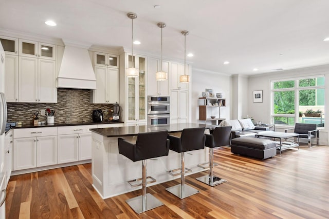 kitchen with custom exhaust hood, white cabinets, decorative light fixtures, a kitchen island, and stainless steel double oven