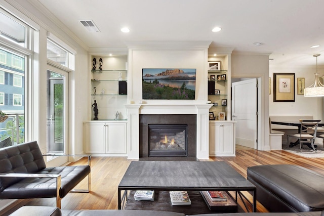 living room featuring built in shelves, light wood-type flooring, and ornamental molding