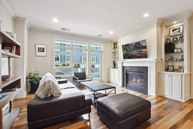 living room featuring built in shelves, light wood-type flooring, and crown molding