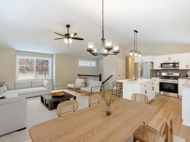 dining space featuring light wood-type flooring, ceiling fan with notable chandelier, vaulted ceiling, and a wealth of natural light