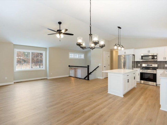 kitchen with white cabinetry, hanging light fixtures, lofted ceiling, a kitchen island, and appliances with stainless steel finishes