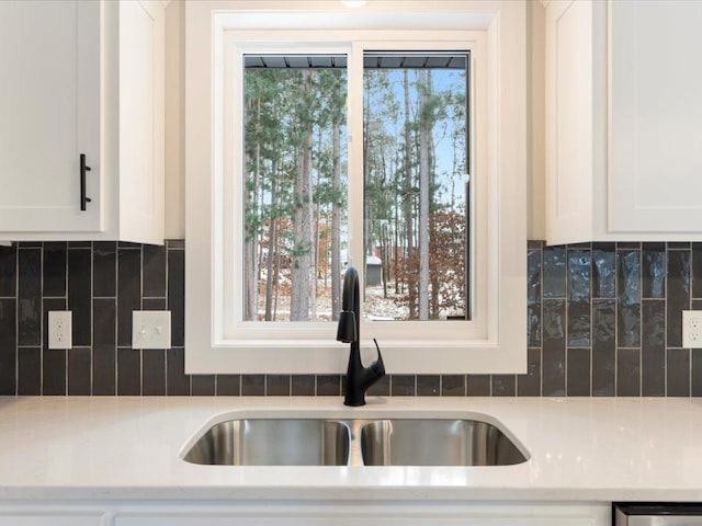 interior details with tasteful backsplash, white cabinetry, and sink