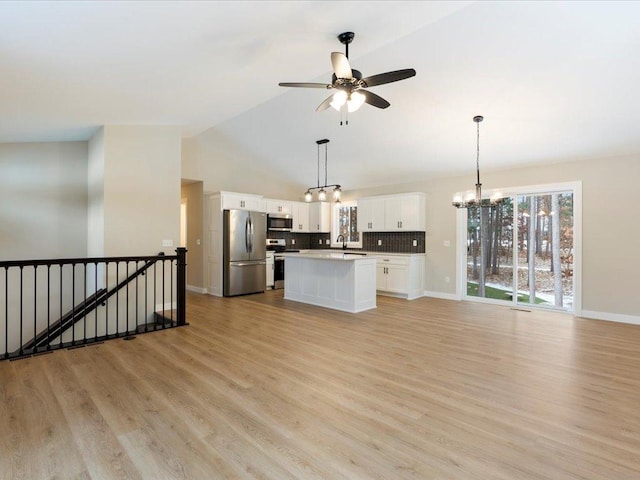 kitchen with stainless steel appliances, a kitchen island, backsplash, vaulted ceiling, and white cabinets