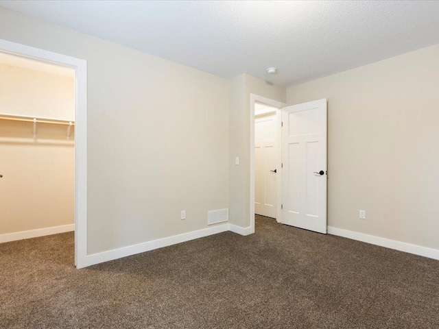 unfurnished bedroom with dark colored carpet, a walk in closet, visible vents, and baseboards