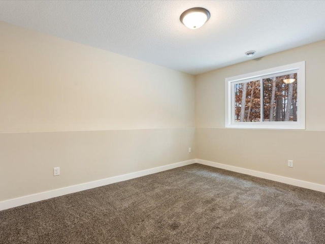 spare room featuring baseboards, dark carpet, and a textured ceiling