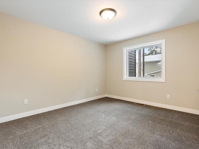 unfurnished room with visible vents, dark carpet, and baseboards