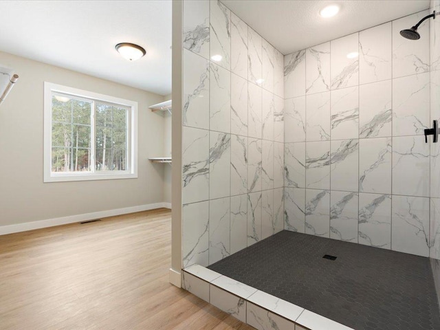 bathroom with wood finished floors, a tile shower, visible vents, and baseboards