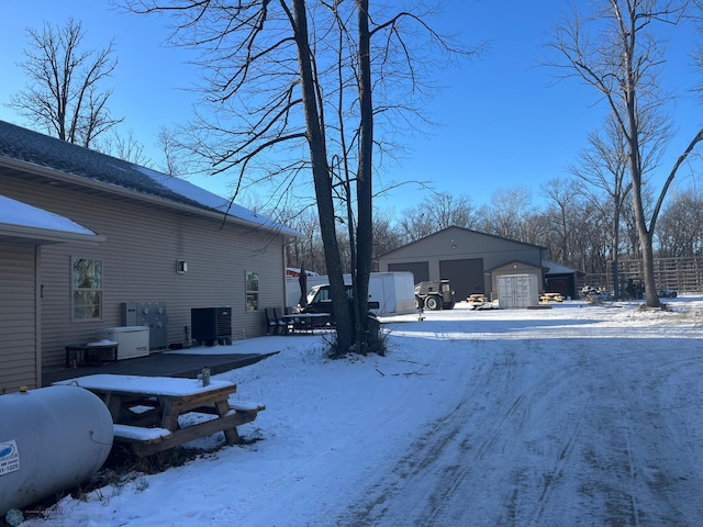 yard covered in snow featuring central AC, an outbuilding, and a garage