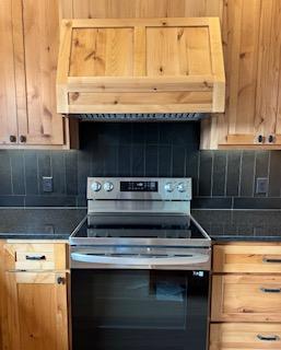 kitchen featuring stainless steel electric range, light brown cabinets, decorative backsplash, and premium range hood