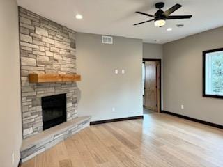 unfurnished living room featuring baseboards, visible vents, a ceiling fan, a stone fireplace, and wood finished floors