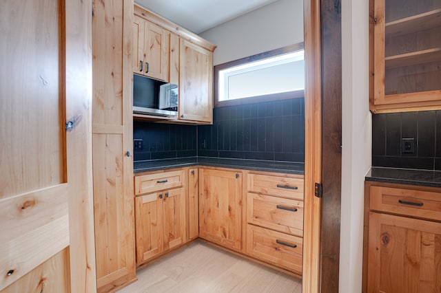 kitchen with backsplash, light brown cabinetry, stainless steel microwave, dark countertops, and light wood-style floors