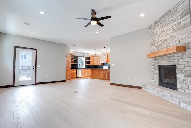 unfurnished living room featuring a ceiling fan, light wood finished floors, a stone fireplace, baseboards, and recessed lighting