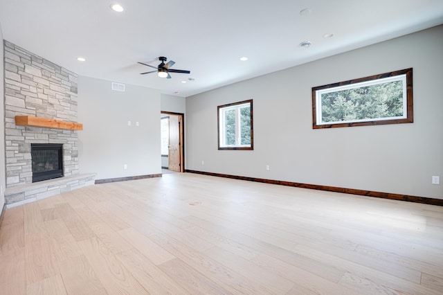 unfurnished living room featuring visible vents, baseboards, a ceiling fan, a stone fireplace, and light wood-type flooring