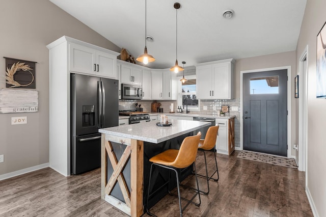 kitchen with lofted ceiling, a kitchen island, white cabinets, and appliances with stainless steel finishes