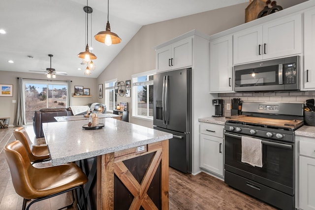 kitchen featuring appliances with stainless steel finishes, decorative light fixtures, tasteful backsplash, white cabinetry, and lofted ceiling