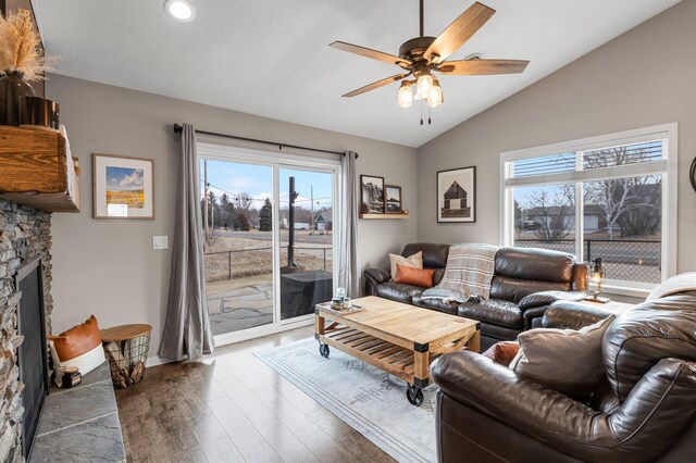 living room with wood-type flooring, lofted ceiling, a stone fireplace, and ceiling fan