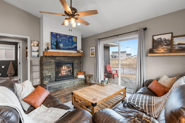 living room with hardwood / wood-style floors, a stone fireplace, vaulted ceiling, and ceiling fan