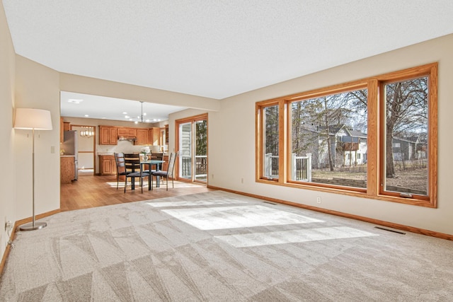 living area with light carpet, an inviting chandelier, visible vents, and baseboards