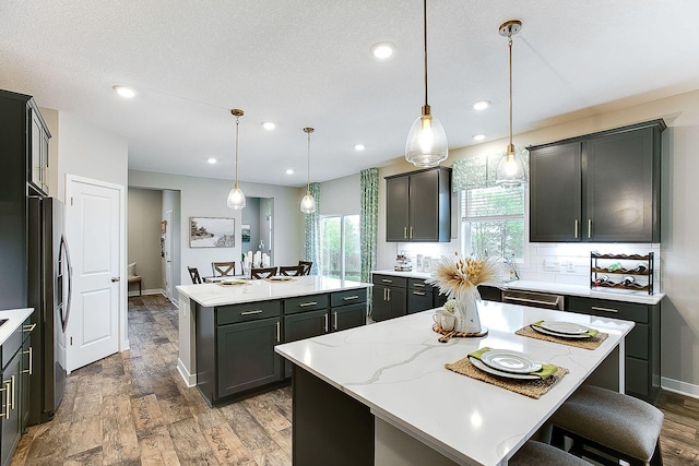 kitchen featuring a center island, hardwood / wood-style flooring, decorative light fixtures, light stone counters, and stainless steel appliances