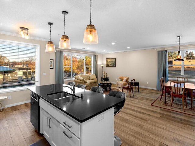 kitchen featuring sink, a center island with sink, dishwasher, white cabinets, and hanging light fixtures