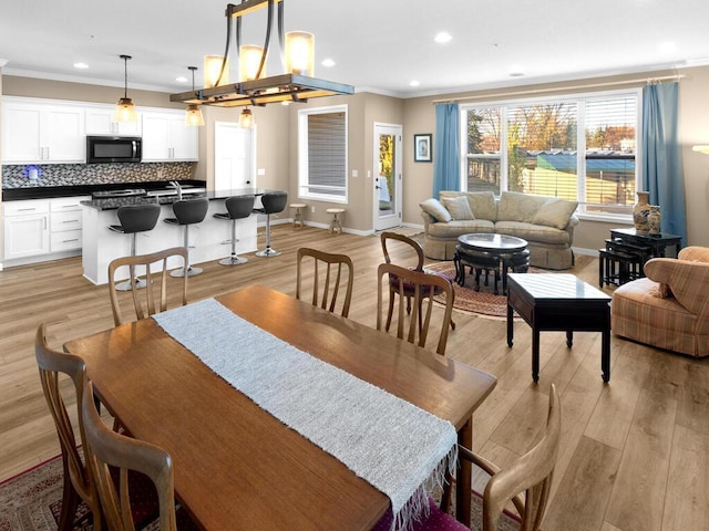 dining area featuring light wood-type flooring, ornamental molding, sink, and a chandelier