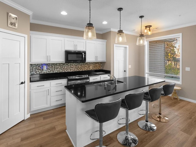 kitchen featuring white cabinets, a kitchen island with sink, sink, and hanging light fixtures