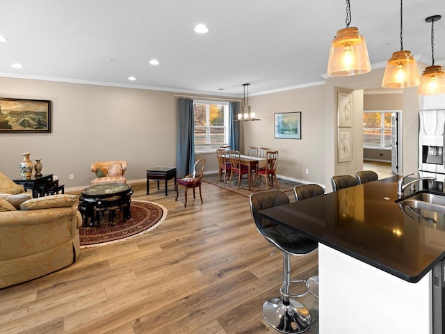 living room featuring sink, light hardwood / wood-style flooring, an inviting chandelier, and ornamental molding