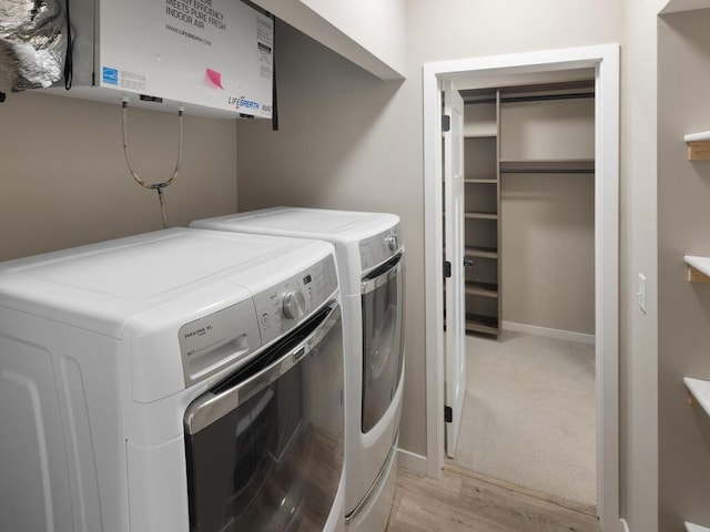 clothes washing area with washer and dryer, light hardwood / wood-style floors, and water heater