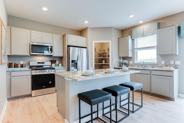 kitchen featuring light wood-type flooring, light stone counters, appliances with stainless steel finishes, a kitchen island, and a kitchen bar