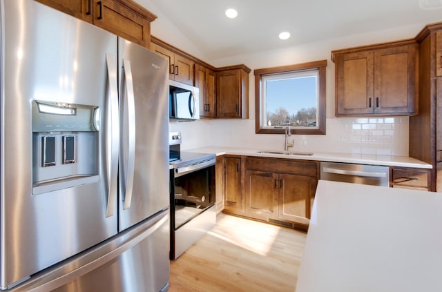 kitchen featuring lofted ceiling, sink, light hardwood / wood-style flooring, appliances with stainless steel finishes, and backsplash