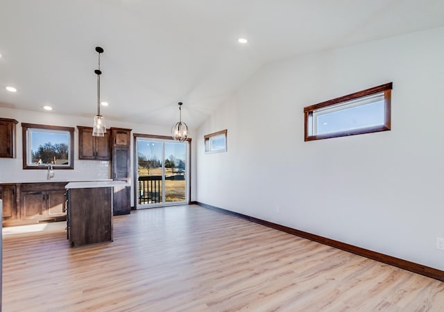 interior space with lofted ceiling, light hardwood / wood-style flooring, a kitchen breakfast bar, a center island, and decorative light fixtures