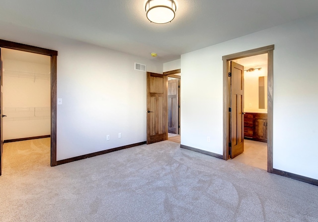 unfurnished bedroom featuring a closet, ensuite bathroom, a spacious closet, and light carpet