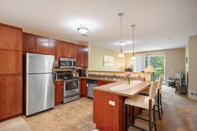 kitchen featuring kitchen peninsula, appliances with stainless steel finishes, a breakfast bar, sink, and decorative light fixtures