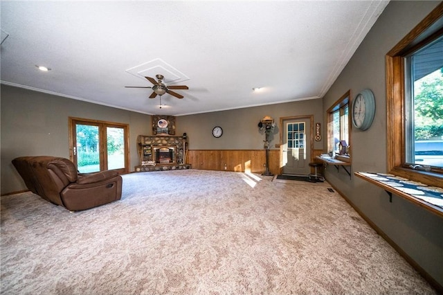 living room featuring ceiling fan, wood walls, light carpet, a fireplace, and ornamental molding