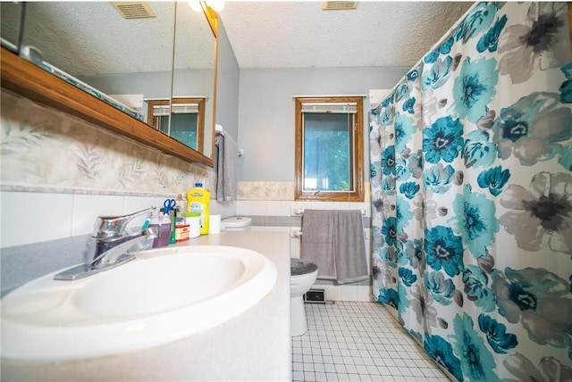 bathroom with a textured ceiling, sink, tile walls, tile patterned flooring, and toilet