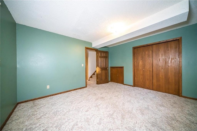 unfurnished bedroom with beam ceiling, light colored carpet, a textured ceiling, and a closet