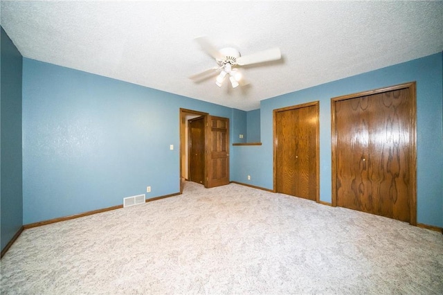 unfurnished bedroom with light carpet, a textured ceiling, two closets, and ceiling fan