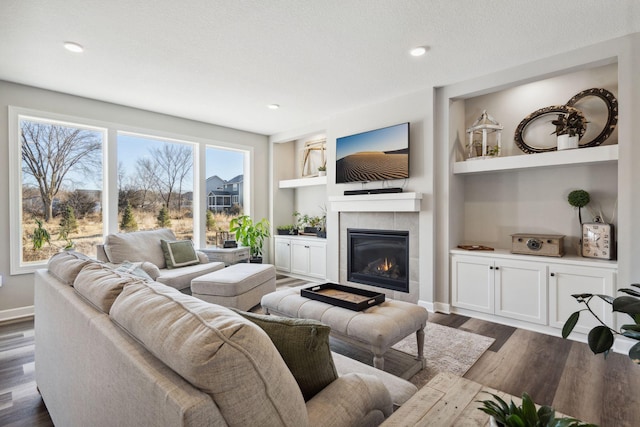 living room with a textured ceiling, built in features, dark wood-type flooring, and a tiled fireplace