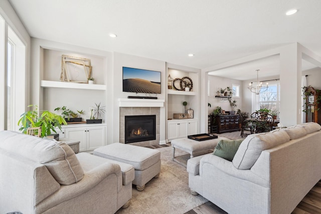 living room with built in shelves, light hardwood / wood-style flooring, a tile fireplace, and a notable chandelier