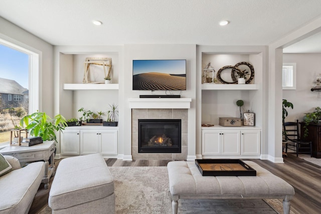 living room with dark hardwood / wood-style floors, a healthy amount of sunlight, built in features, and a tiled fireplace