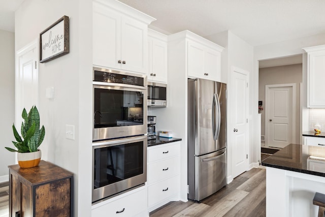 kitchen with decorative backsplash, white cabinetry, light wood-type flooring, and appliances with stainless steel finishes