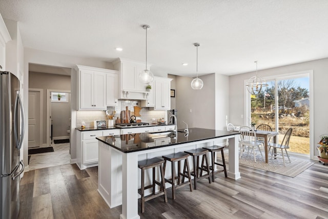 kitchen featuring appliances with stainless steel finishes, backsplash, a kitchen island with sink, decorative light fixtures, and white cabinetry