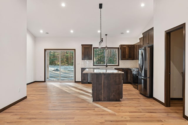 kitchen featuring light wood-type flooring, tasteful backsplash, decorative light fixtures, a center island, and stainless steel refrigerator