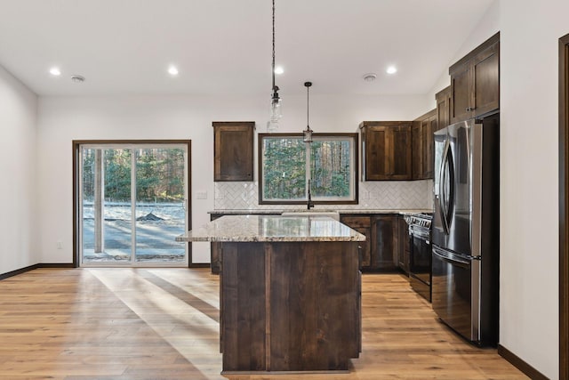 kitchen with light stone counters, pendant lighting, black gas stove, a center island, and stainless steel refrigerator