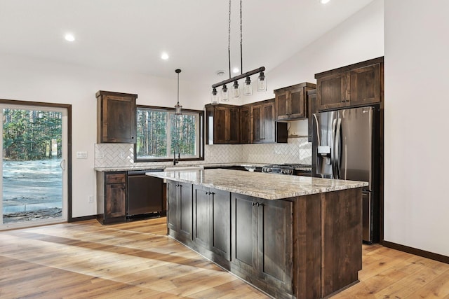 kitchen with light stone counters, stainless steel appliances, vaulted ceiling, pendant lighting, and a center island