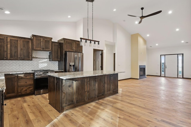 kitchen featuring appliances with stainless steel finishes, tasteful backsplash, decorative light fixtures, a kitchen island, and light stone counters