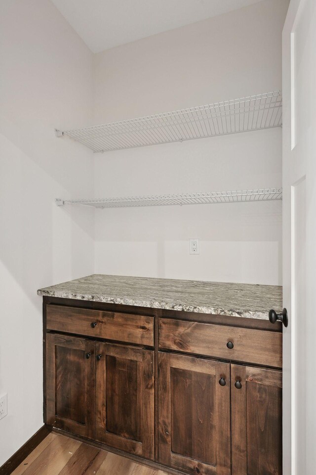 bar featuring light stone countertops, dark brown cabinets, and light wood-type flooring